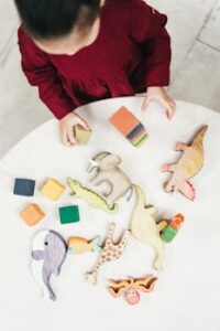 A young girl in a red dress playing with wooden animal toys on a round table, viewed from above.